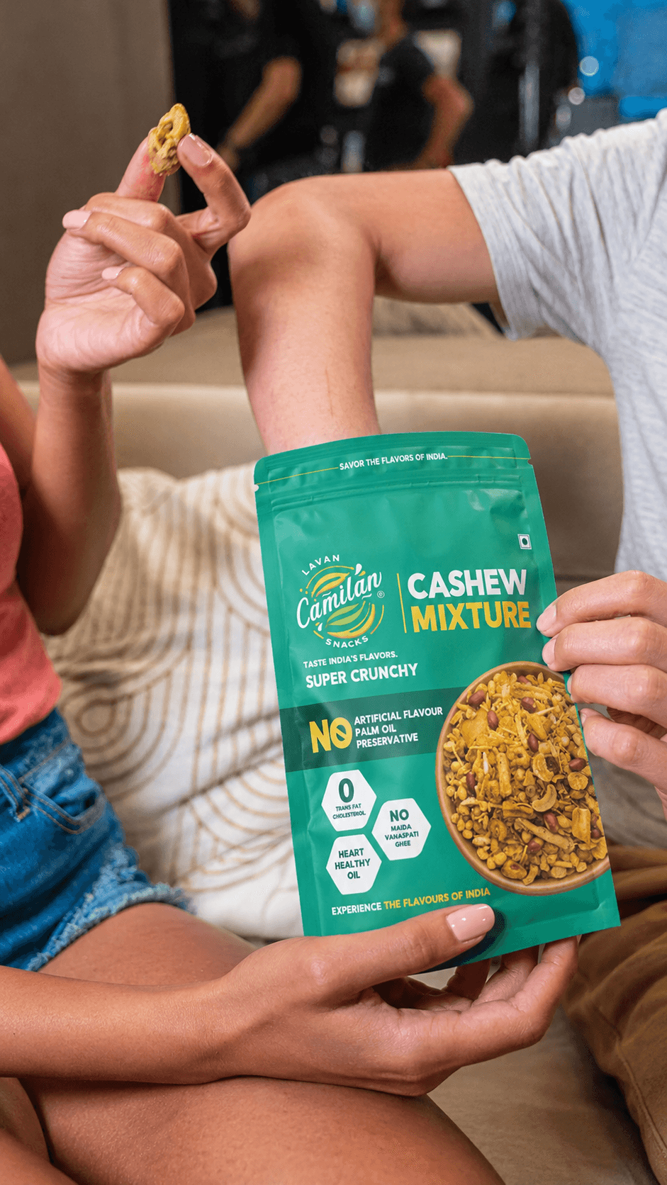 Person relaxing on a sofa holding a Cashew Mixture pouch while sharing a handful